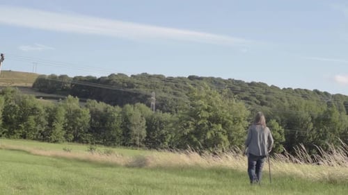 Woman Walking with Stick Through Grassy Field
