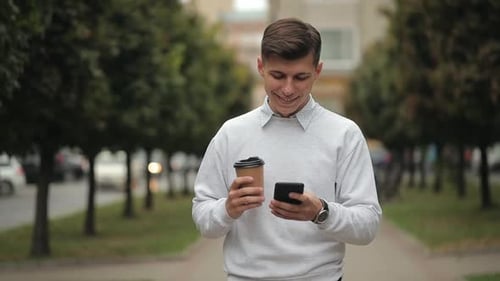 Young Man Walks with Coffee and Smartphone