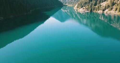 The emerald water of the mountain lake displays coniferous forest, autumn grass, passing clouds.