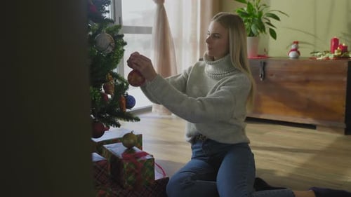 Woman Decorates Christmas Tree with Ornaments at Home
