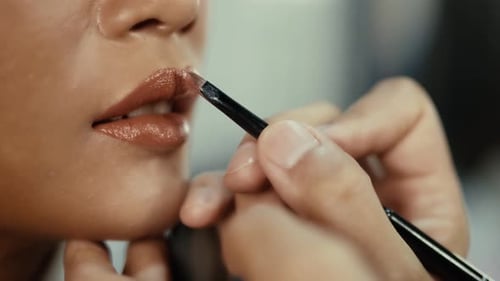 Professional makeup artist putting lipstick on a model's lips in the studio