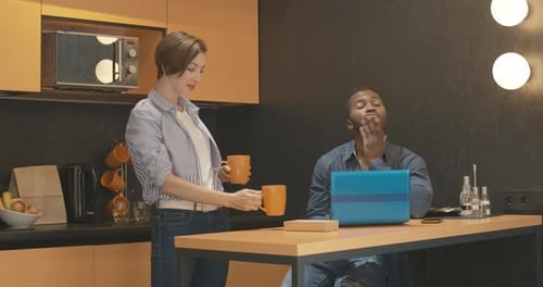 Woman Offers Mug to Man Working on Laptop