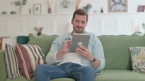 Man Celebrates Success Using Tablet at Home
