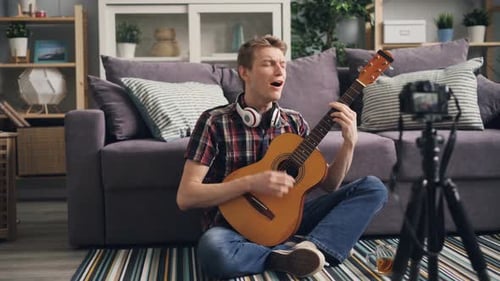 Male Recording Himself Playing Guitar and Singing Indoors