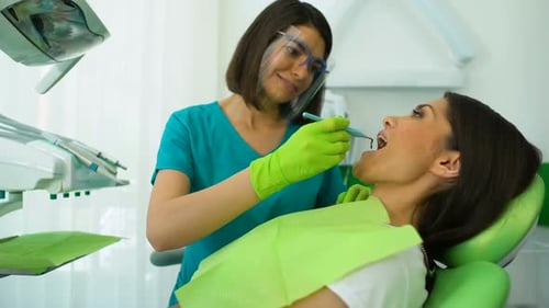 Dentista calificado que examina los dientes de la mujer, chequeo regular en clínica moderna