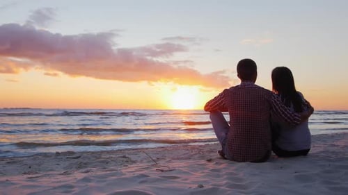 Young Romantic Couple Sitting on the Beach, Admiring the Sunset