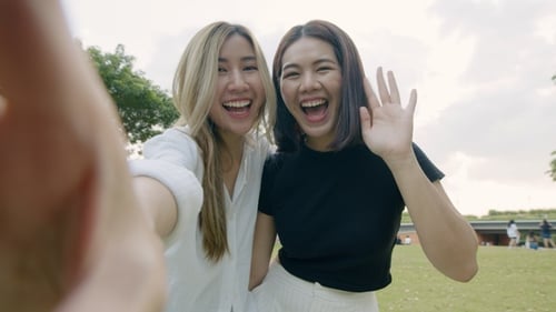 Two Women Smiling and Waving in a Park