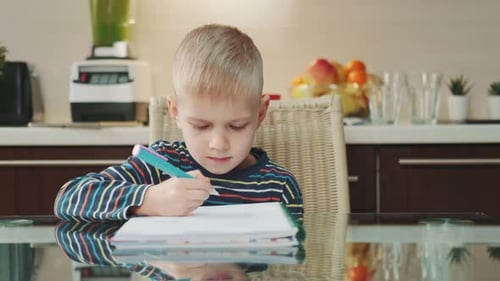Young Boy Drawing in Notebook at Kitchen Table