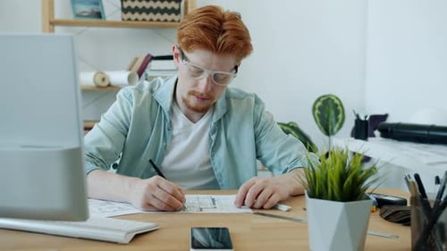 Ralenti d'un jeune architecte dessinant sur un plan de construction et utilisant un ordinateur au bureau