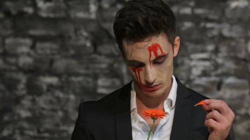 Man with Halloween Makeup Plucking Orange Flower