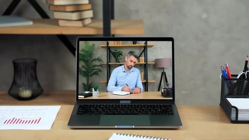 Laptop Standing on Table Display with Businessman in Office Writes in Notebook