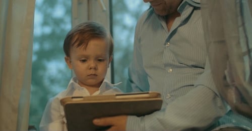 Child and Man Use Tablet Together Indoors