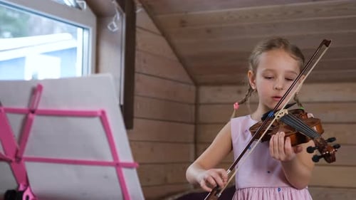 Young Girl Plays Violin at Home with Music Stand