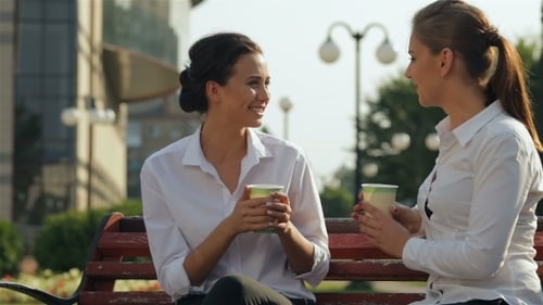 Two Young Women Chatting Over Coffee in Park