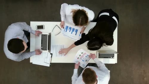 Junge Büromitarbeiter bringen Laptops und Papiere an den Schreibtisch