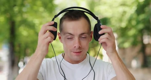 Smiling Man Puts on Big Headphones in the Summer City
