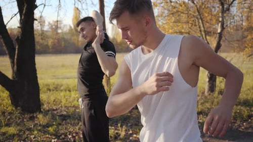 Two Caucasian Sportsmen Warming Up in the Autumn Park. Strong Adult Boys Stretching Before