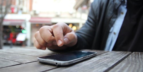 Hand Using Silver Smartphone on Wooden Table