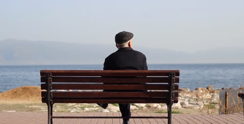 Senior Man Relaxes on Bench Overlooking the Sea