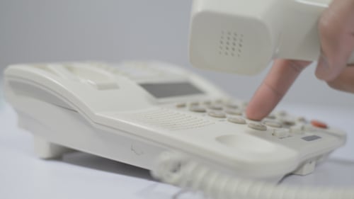Finger Dials Number on a White Office Phone