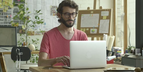Man With Glasses Works on Laptop at Desk