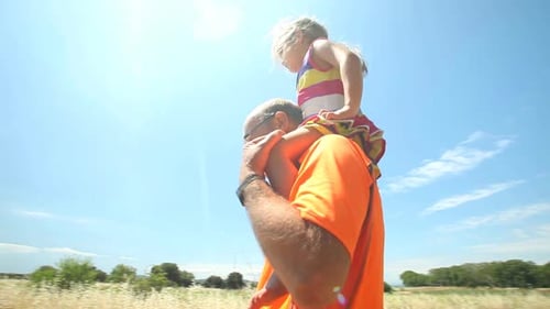 Grandfather Carries Granddaughter on Shoulders Through Grassy Field