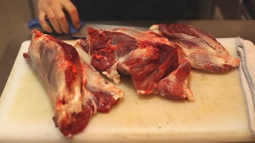 Hands Cutting Raw Meat with Knife in Kitchen