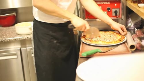 Man Cutting Pizza With Pizza Cutter in Kitchen