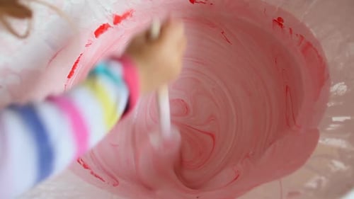 Child Mixing Red and White Icing in Bowl
