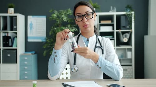 Portrait of Cheerful Female Doctor Talking Smiling Showing Pills in Hospital Office