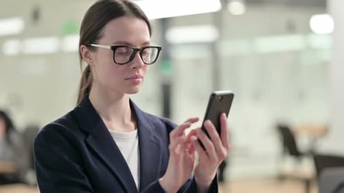 Serious Young Woman Using Smartphone in Modern Office