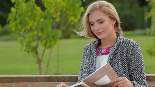 Blonde Woman Reads Book on Park Bench