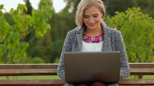 Woman Uses Laptop Sitting in Park on Bench