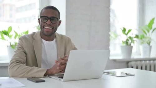 African Man Smiling at Camera While Using Laptop in Office