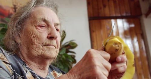 an Elderly Woman a Grandmother an Old Woman Peeling Potatoes with a Knife in Her House a Purposeful