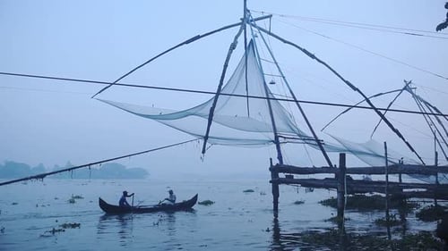 Local people on a boat near traditional chinese fishing nets, Fort Kochi, India, at dusk