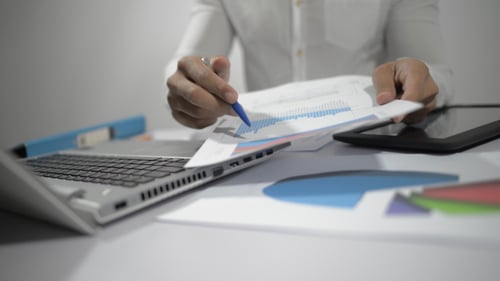 Analyst Working with Charts and Laptop at Desk