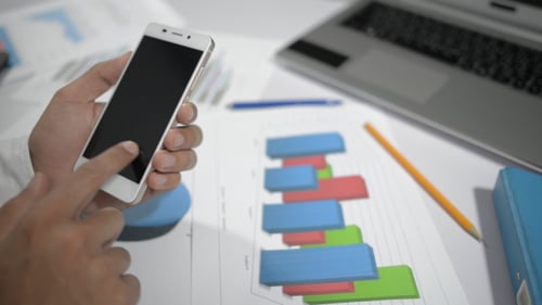 Hands Using Smartphone with Business Charts at Workplace