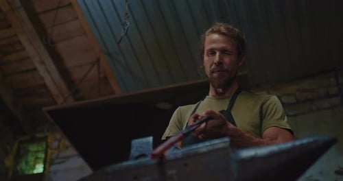 Handsome Blacksmith is Hammering Metal Detail on Anvil Tilt Up Portrait in Workshop Prores