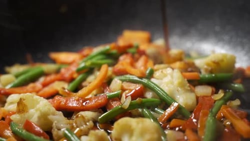 The Chef in the Kitchen Pours Soy Sauce of Vegetables for Wok in a Pan Which is Fried and Stir