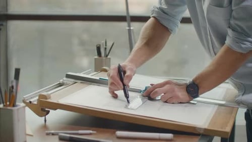 Nahaufnahme von Architektenhänden, die Hauspläne im Büro in der Nähe des Fensters erstellen