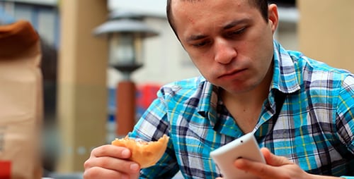 Young Adult Eating Burger While Talking on Phone