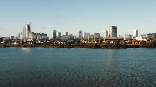 Drone Turning Left Above Beautiful Autumn Lake, Modern Futuristic City Skyline Scenery and Suburbs