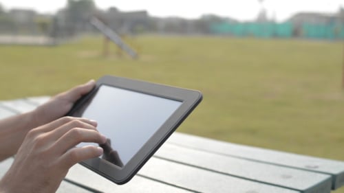 Hands Using Tablet Device on a Picnic Table