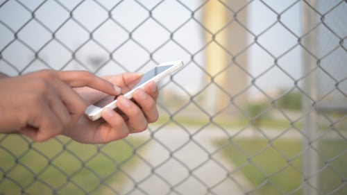 Hand Holding Smartphone with Chain Link Fence