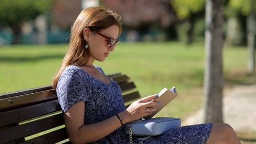 Woman Reading Book on Park Bench in Sunlight