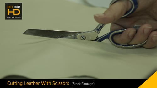 Hand cutting light-tan material with scissors