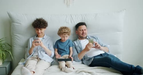 Family Relaxing on Bed with Mobile Devices