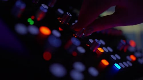 Hand Adjusting Controls on Audio Mixer at Night