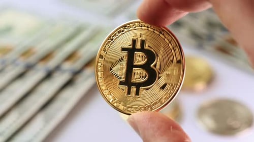 Fingers Holding Bitcoin in Front of Dollar Bills